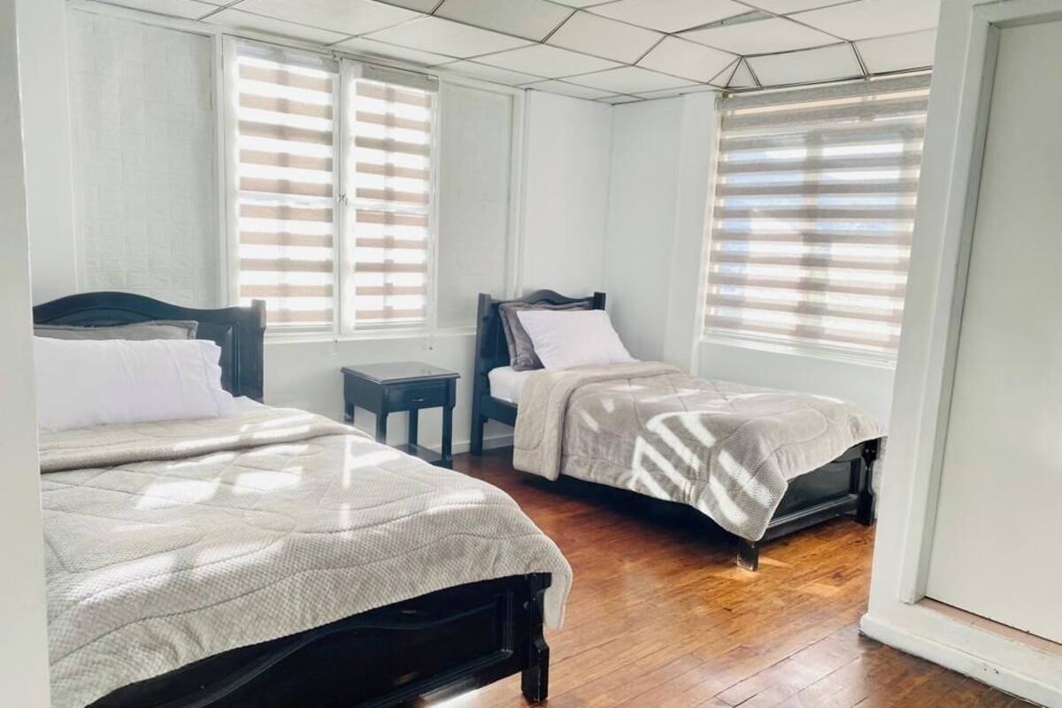 A room with two beds, a small table, and a window with blinds.
