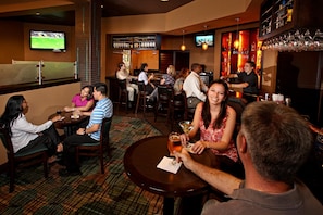 A bar area with multiple seating arrangements, including round tables and bar stools. There are televisions mounted on the walls displaying sports events. - Rosen Inn at Pointe Orlando (Orlando)