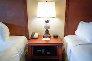 A hotel room with two beds, a bedside table with a lamp, a phone, a digital clock, and a safe.