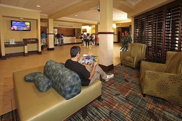 A hotel lobby with a registration desk, seating area, and a television displaying a menu.