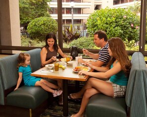 A family dining at a table with a view of greenery and a building in the background. - Rosen Inn at Pointe Orlando (Orlando)