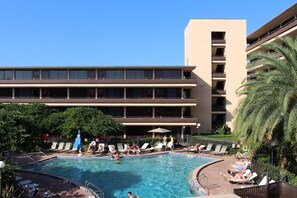 A hotel with a swimming pool, multiple balconies, and a clear blue sky.