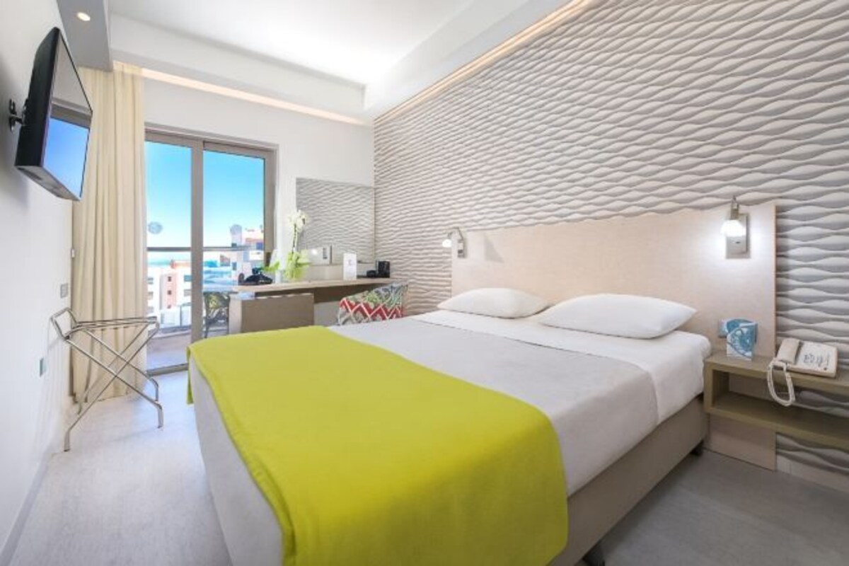 Quarto de hotel moderno com cama, mesa de cabeceira e vista para a cidade.