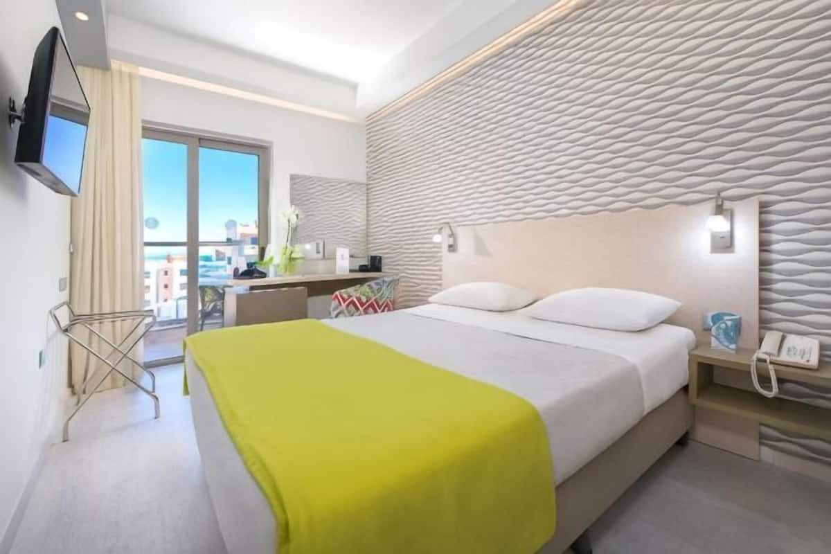 A modern hotel room with a bed, bedside table, and a view of the city.