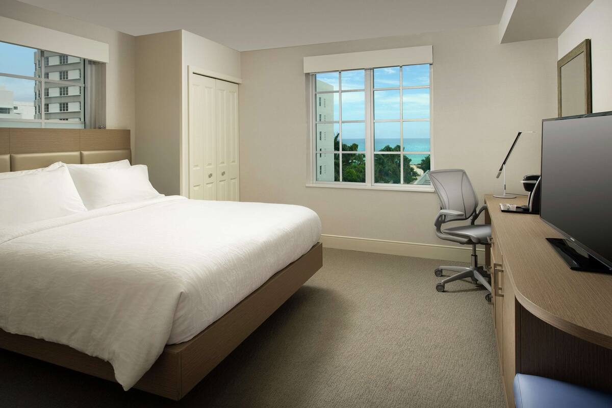 Une chambre d’hôtel avec un lit, un bureau avec un ordinateur, une chaise et une fenêtre donnant sur un paysage agréable.