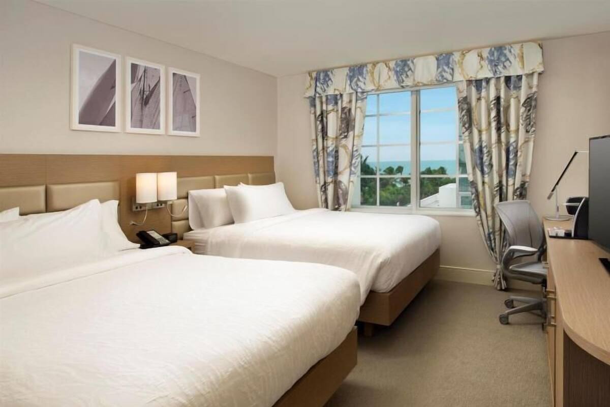 Une chambre d’hôtel avec deux lits, un bureau, une chaise, une télévision et une fenêtre avec des rideaux.