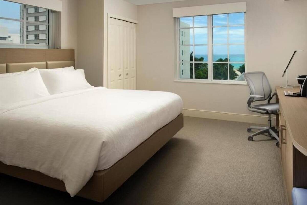 Une chambre d’hôtel équipée d’un lit, d’un bureau, d’une chaise, d’une fenêtre donnant sur un paysage agréable et d’une armoire.