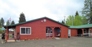 A red log cabin with a porch, a small front window, and a door.