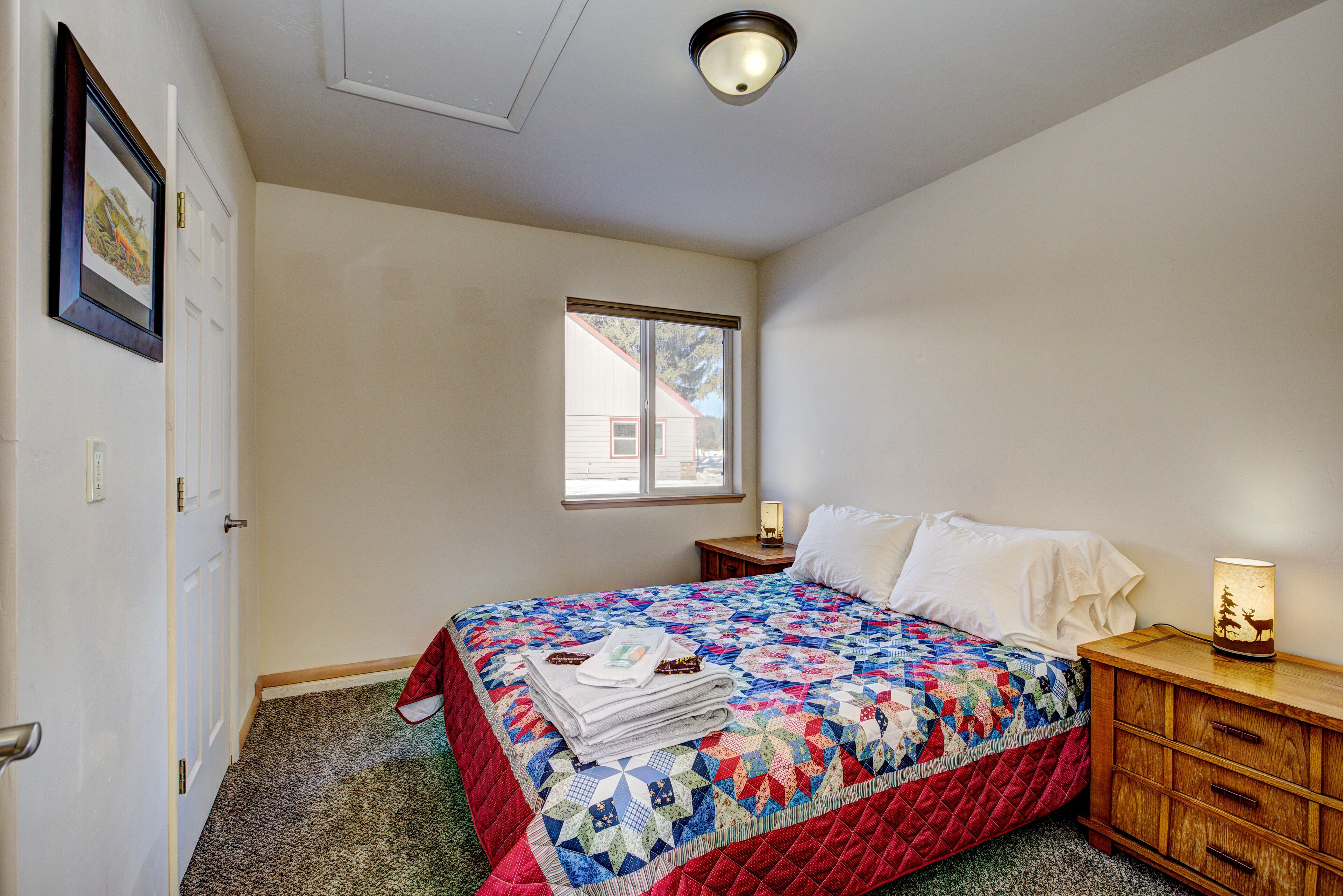 A bedroom with a bed, a nightstand, a lamp, and a window.