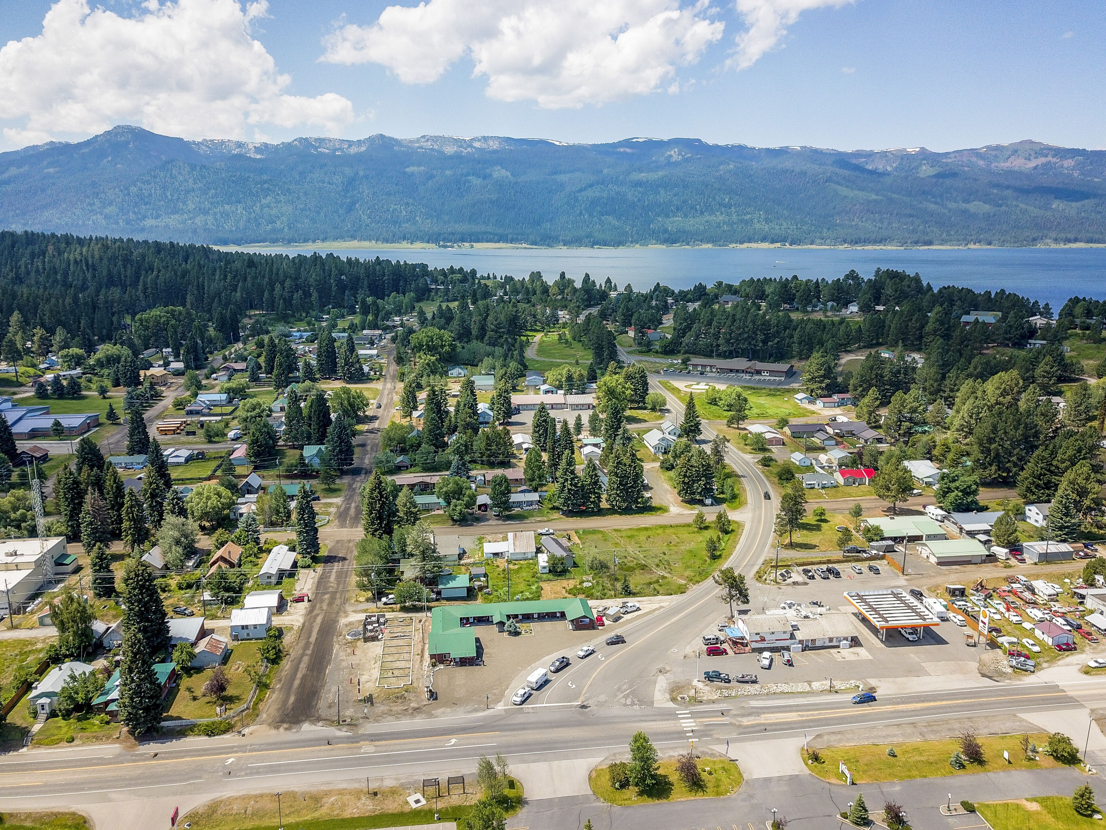 An aerial view of a small town with a main road, a parking lot, and a body of water in the background.