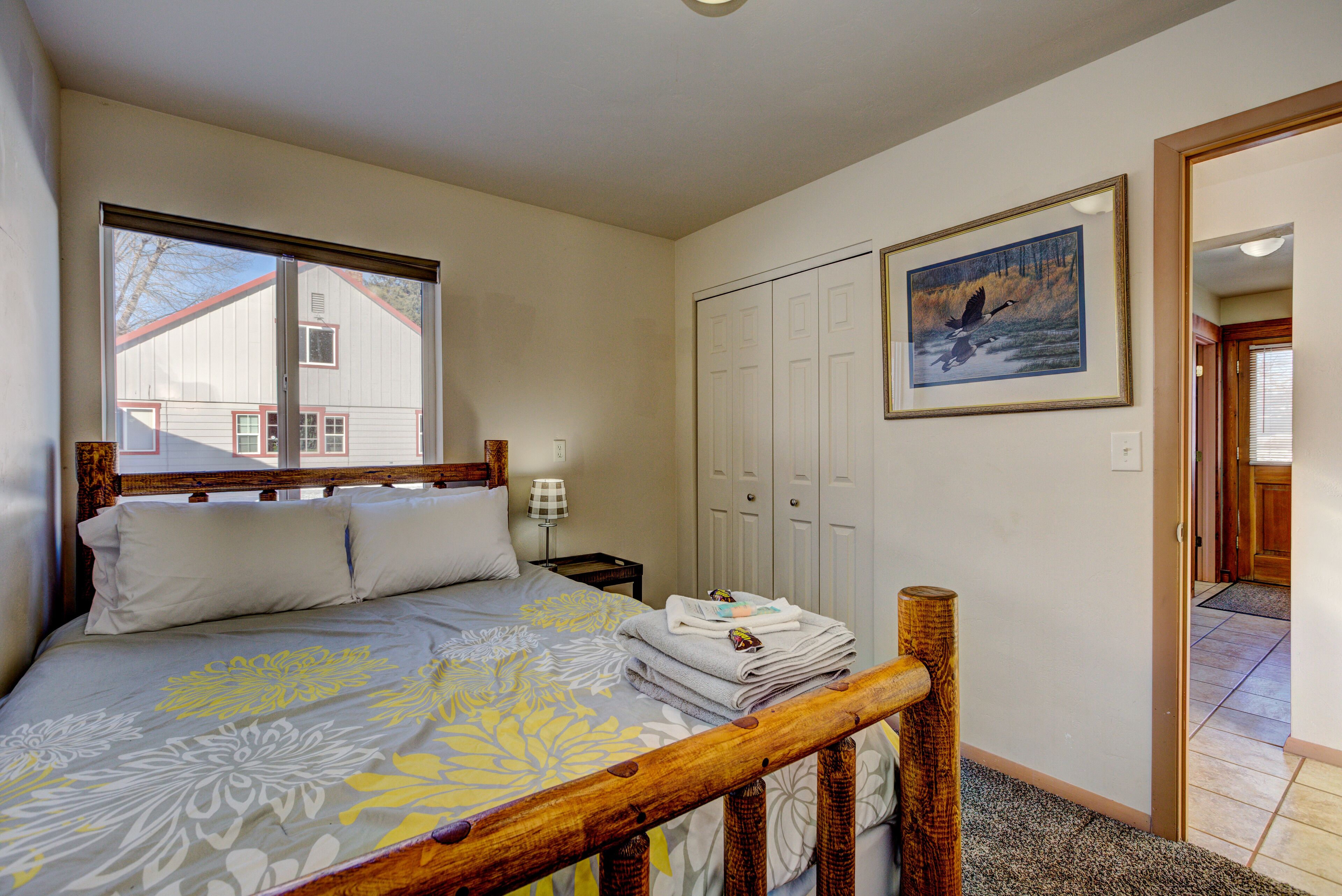 A bedroom with a bed, a nightstand, a wooden headboard, a closet, and a framed picture on the wall.