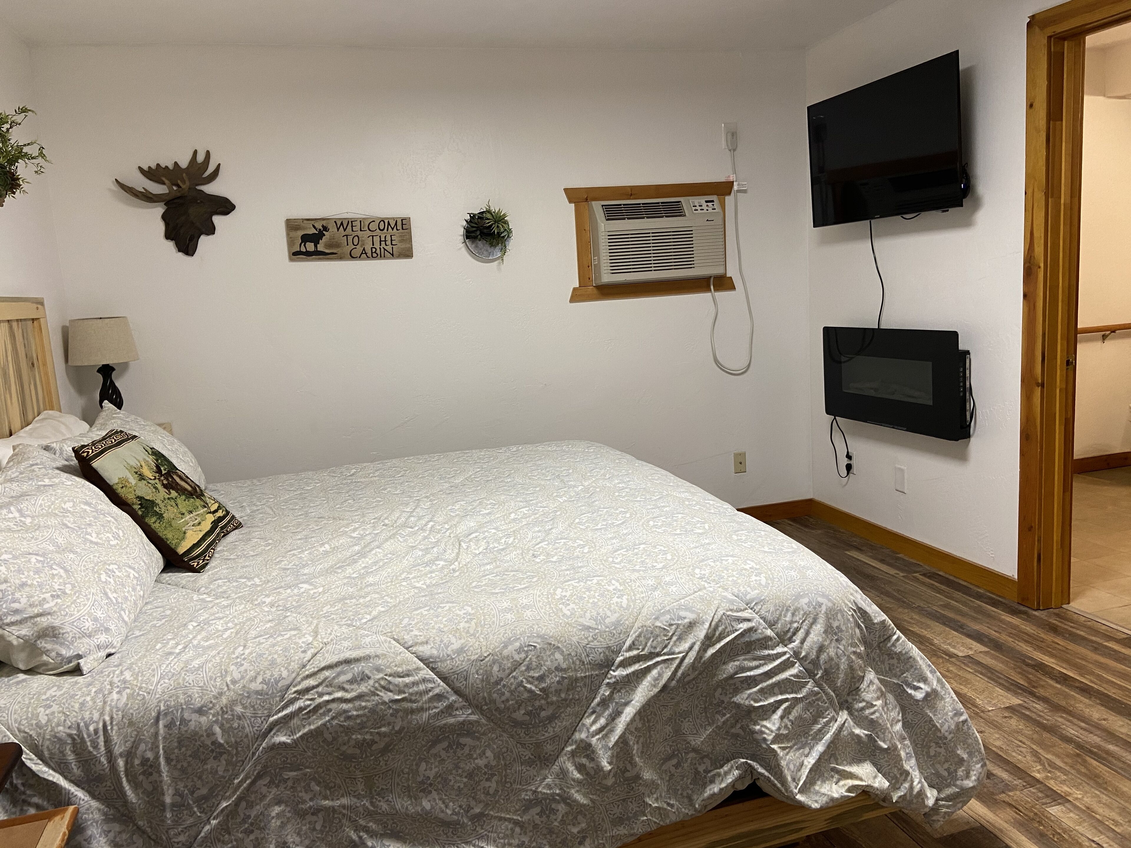 Un dormitorio con cama, televisor montado, aire acondicionado instalado en la pared y un cartel de bienvenida.