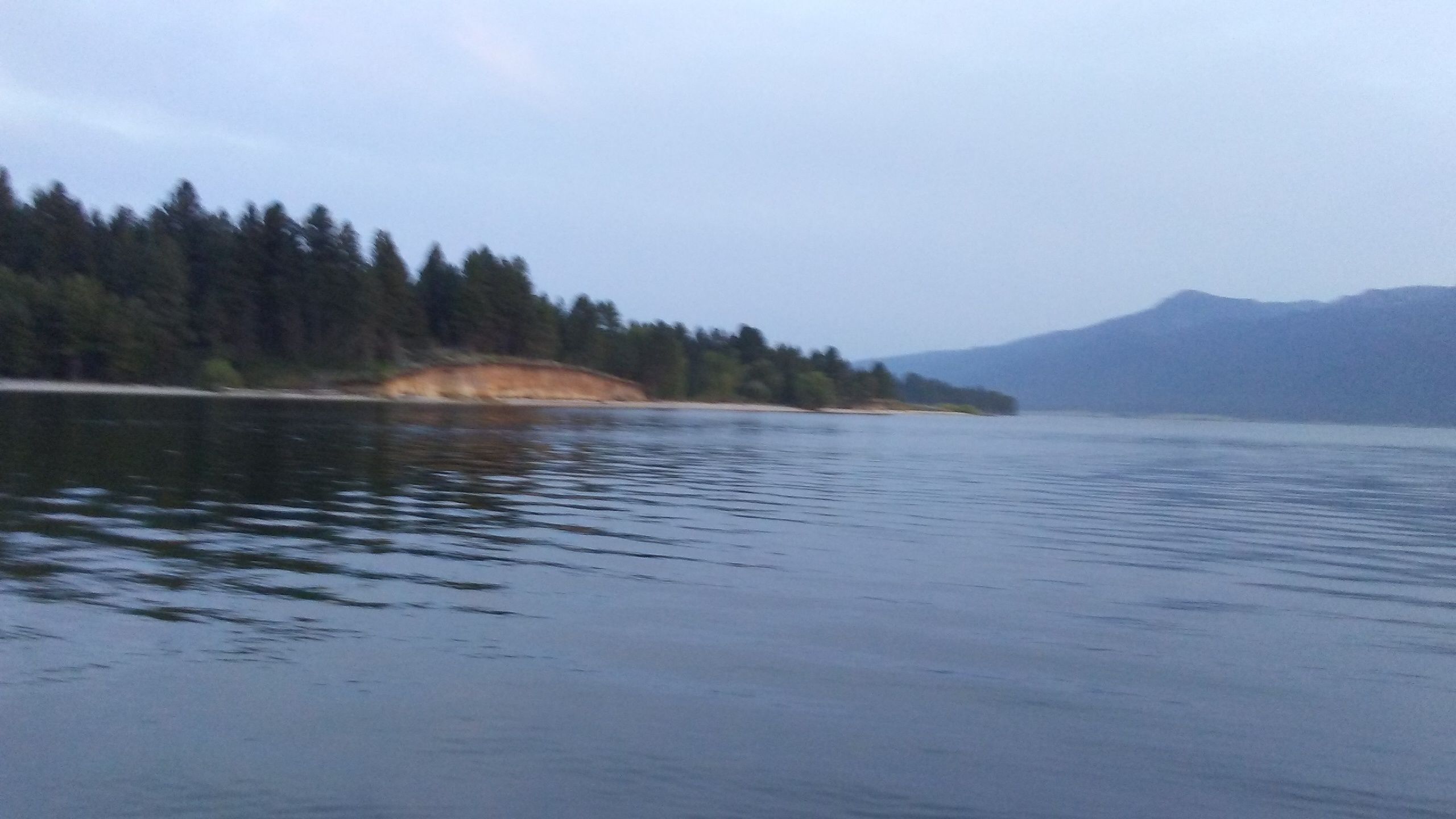 Un lac paisible, bordé d’une forêt et dominé par des montagnes lointaines.