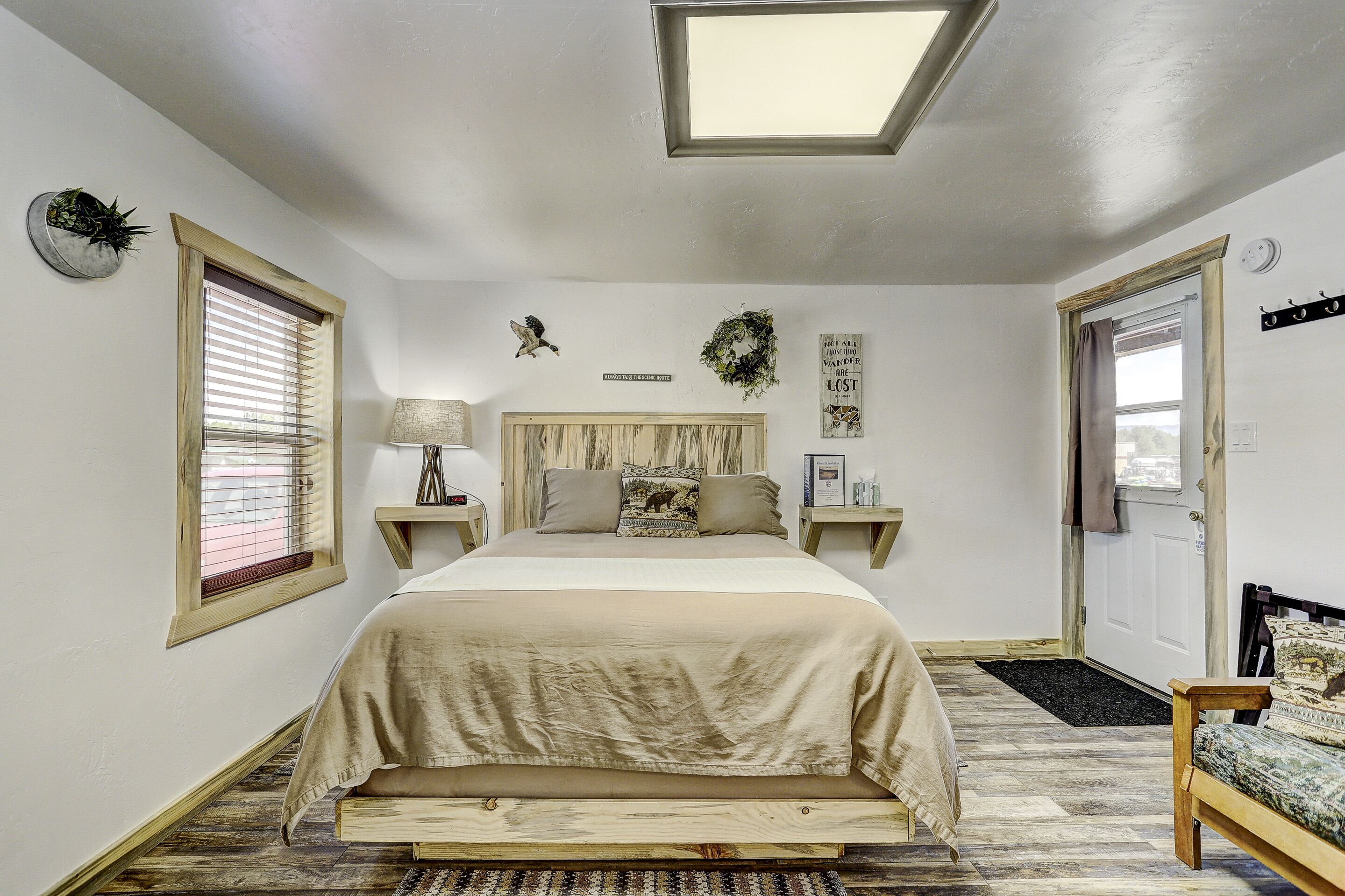 Une chambre à coucher comprenant un lit, des tables de chevet, une commode, une fenêtre avec des stores, une porte et un petit tapis.
