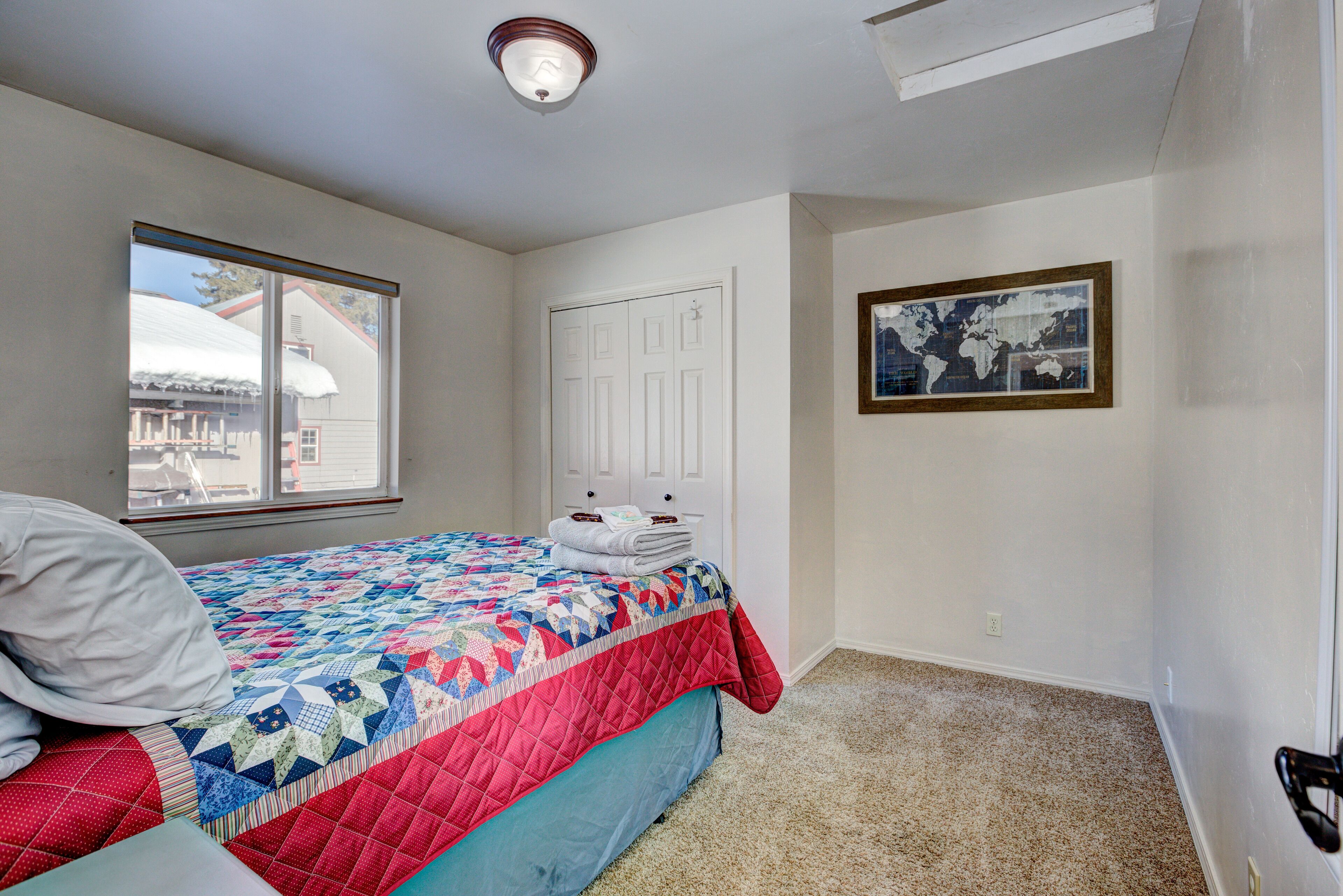 A bedroom with a bed, a window, a door, and a framed picture on the wall.