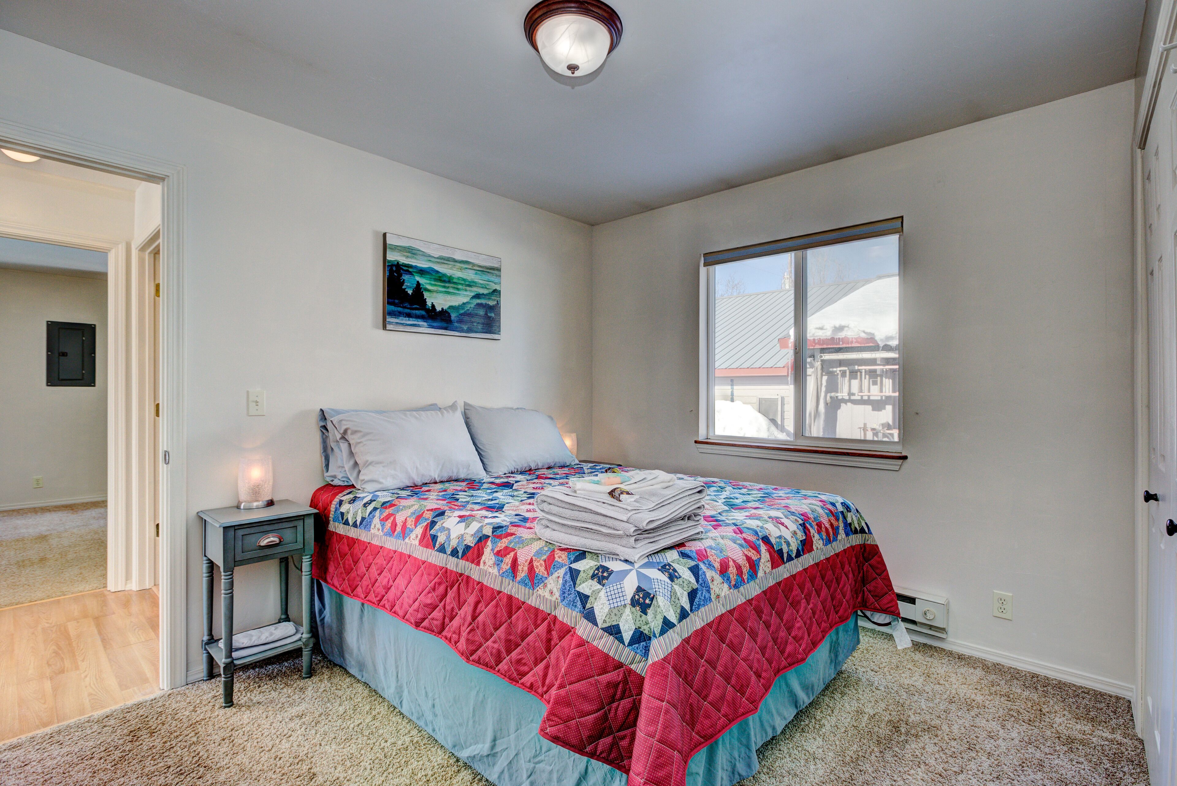 A bedroom with a bed, a nightstand, a window, and a painting on the wall.
