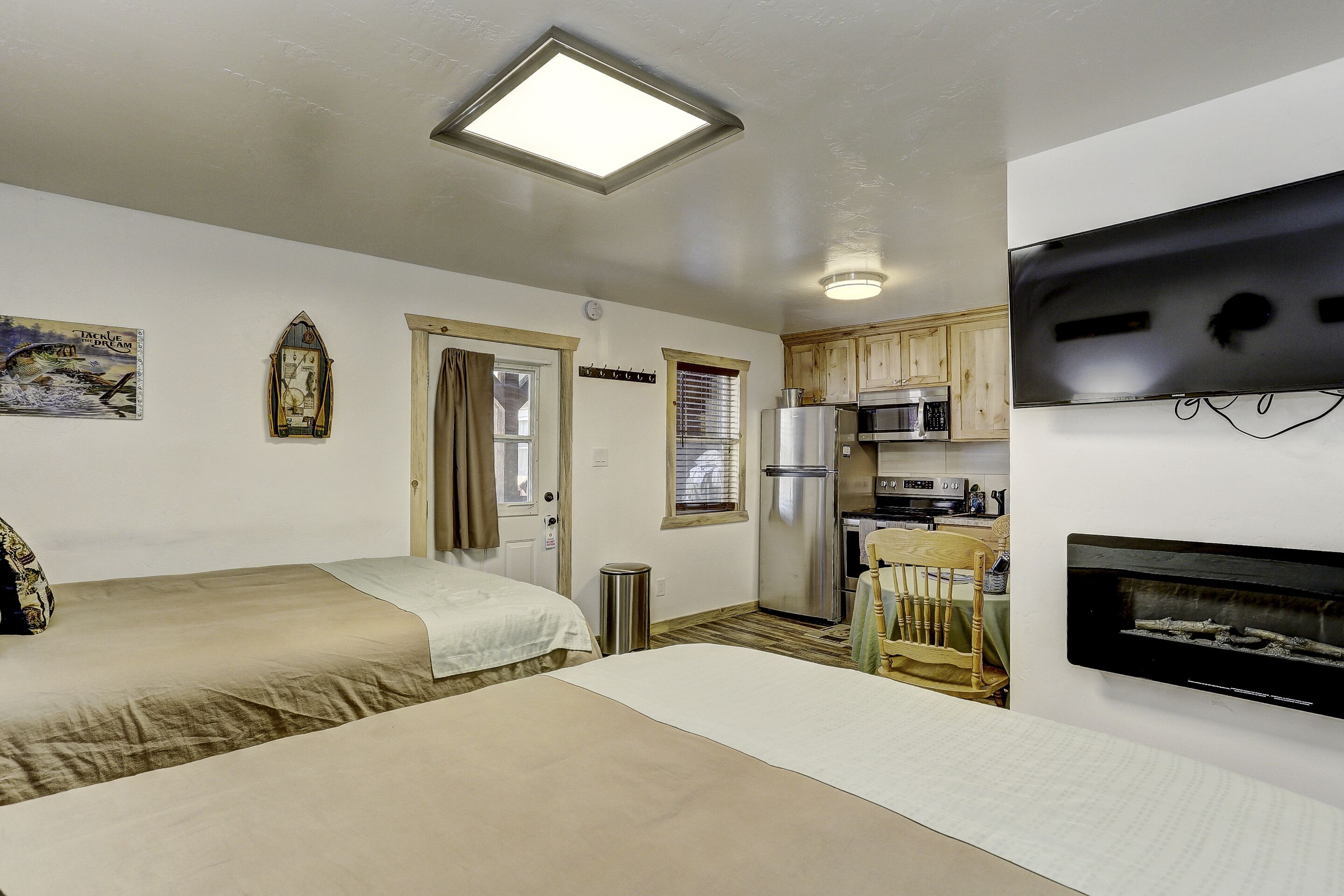A compact room with two beds, a kitchenette, and a flat-screen TV mounted on the wall.