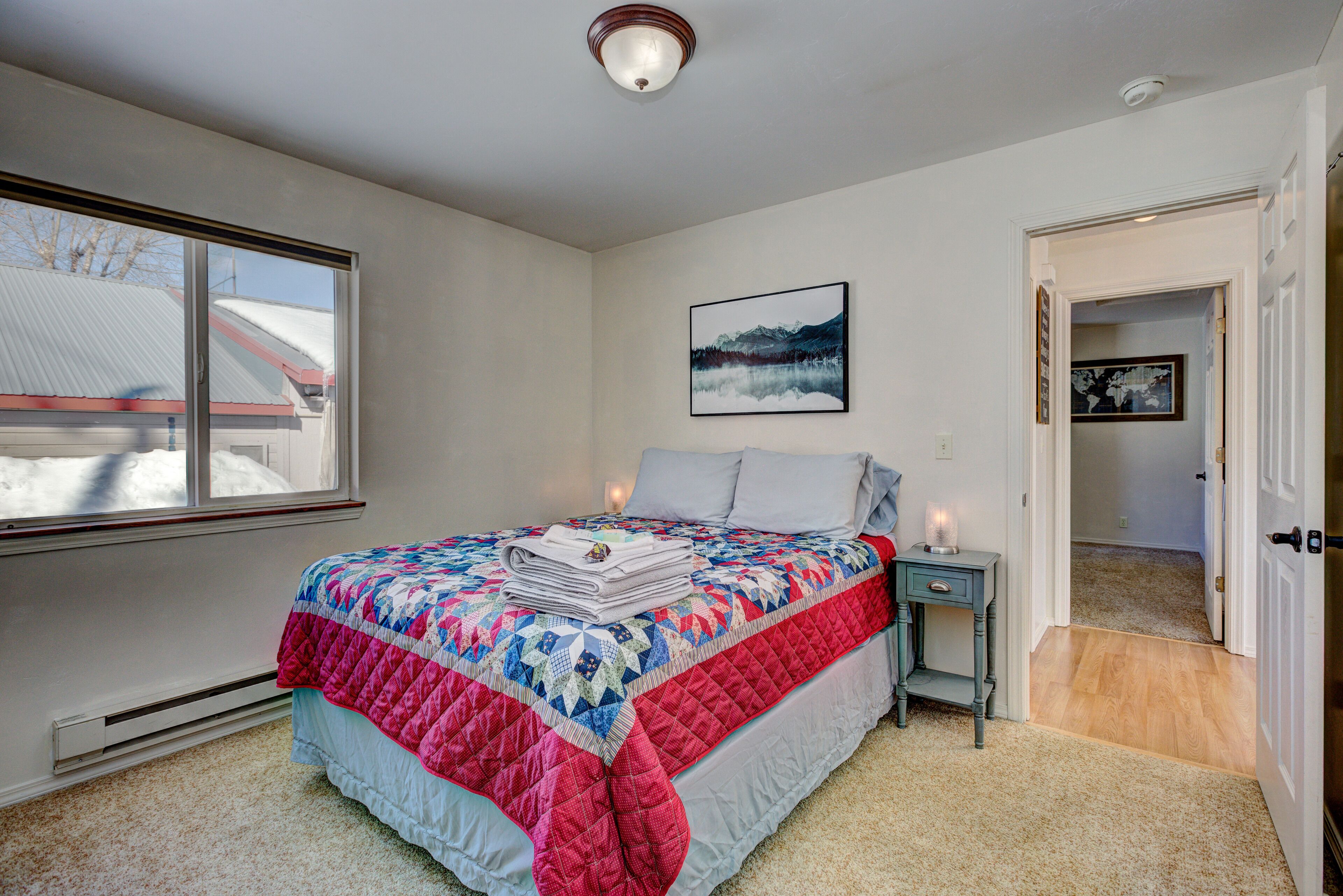 A bedroom with a bed, a nightstand, a window, and a door leading to another room.