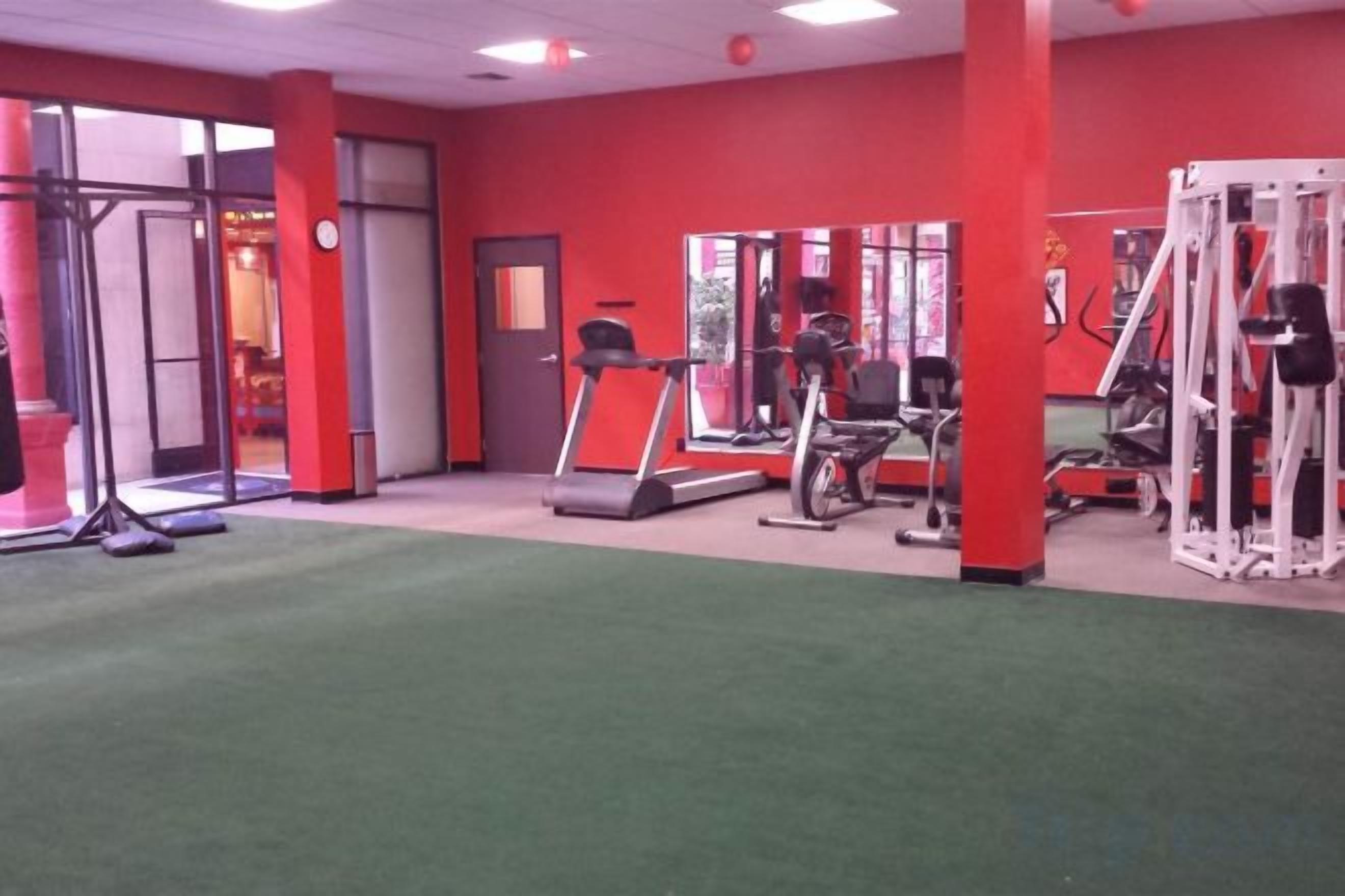 Een sportschool met trainingsapparatuur, een loopband en een spiegelwand.