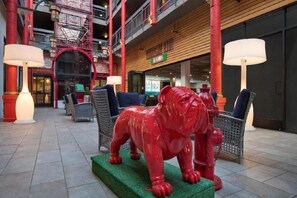 A red sculpture of a bull on a green platform in a lobby with wicker furniture and lamps. - Best Western Plus Dragon Gate Inn (Los Angeles)