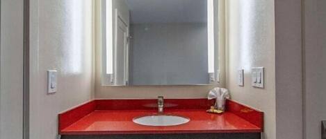 A bathroom with a red countertop, a white sink, and a mirror above it.