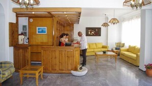 A reception area with wooden paneling, a reception desk, yellow sofas, and hanging lamps. - Kamari Blue Boutique Hotel (Santorini)
