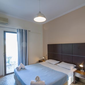 Een hotelkamer met een bed, nachtkastje, lamp, plafondlamp, een raam met gordijnen en uitzicht op het exterieur.