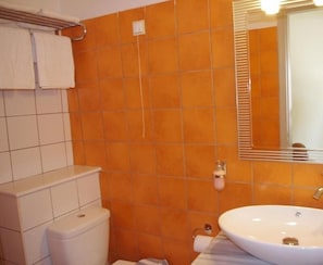 Un baño con baldosas naranjas, un inodoro blanco, un lavabo y un espejo.