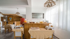A dining area with a wooden counter, a buffet table, and a kitchen in the background. - Kamari Blue Boutique Hotel (Santorini)