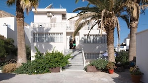 A white building with a staircase leading to a door, surrounded by palm trees and potted plants. - Kamari Blue Boutique Hotel (Santorini)