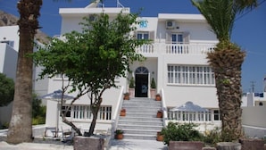 A white building with a staircase leading to the entrance, surrounded by palm trees and potted plants. - Kamari Blue Boutique Hotel (Santorini)