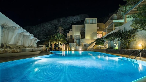 A swimming pool with a clear blue water surface, surrounded by a modern building with multiple balconies and a staircase leading to an upper level. - Antinea Suites And Spa (Santorini)