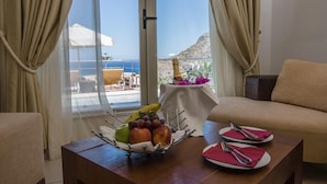 A room with a view of the sea, a table with fruit and cutlery, and a sofa. - Antinea Suites And Spa (Santorini)