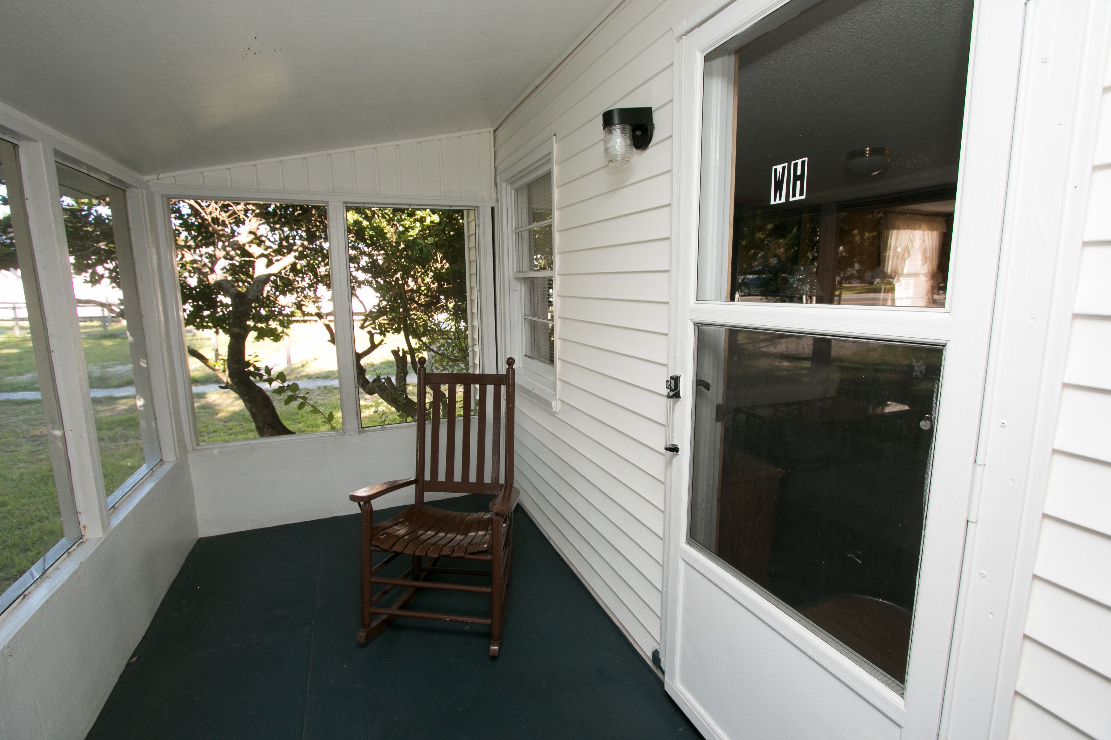 A covered porch with a wooden rocking chair, large windows, and a door with a 'WH' sign.