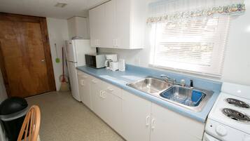 A compact kitchen with white cabinets, a blue countertop, a sink, a microwave, a stove, and a broom.