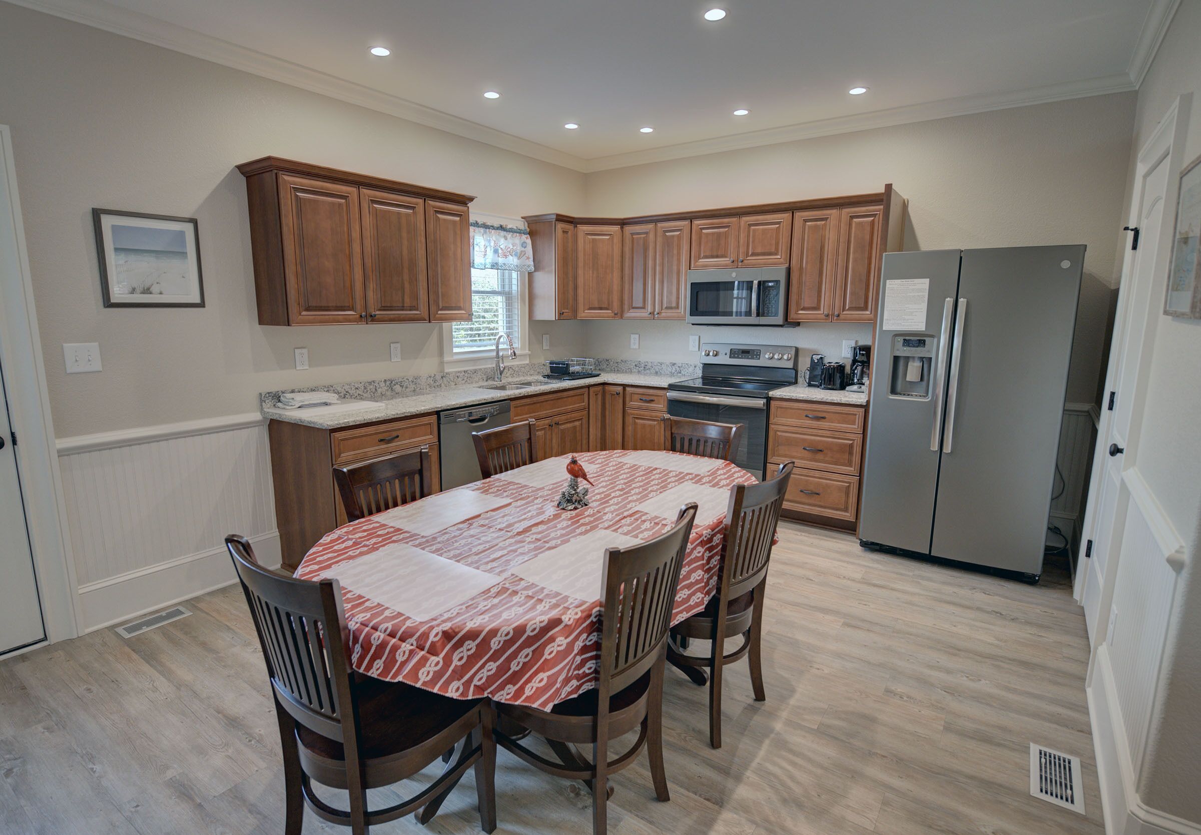 A modern kitchen with wooden cabinets, a granite countertop, a stainless steel refrigerator, and a dining table with chairs.