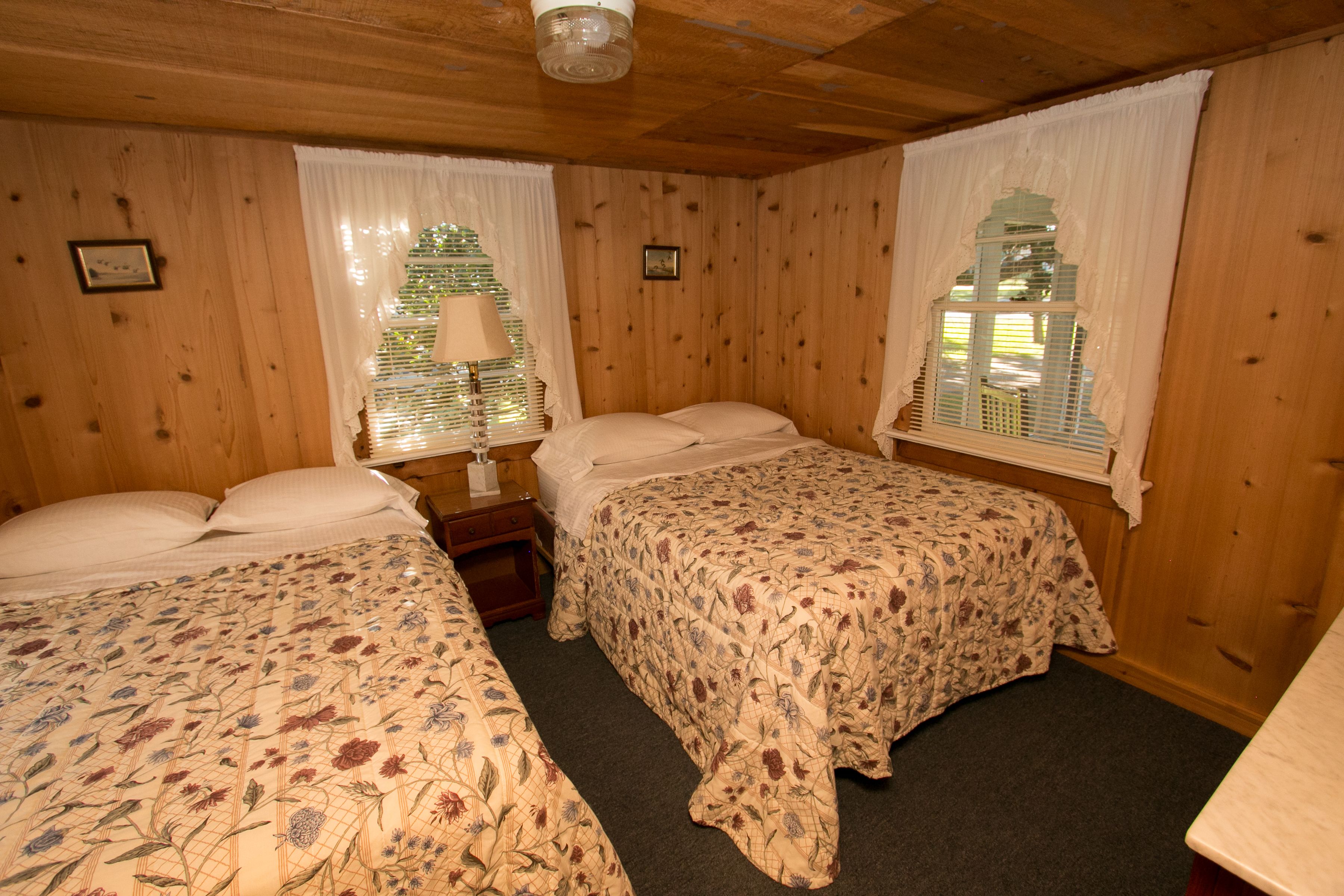 Una stanza con rivestimento in legno, due letti, ognuno con biancheria da letto floreale, un comodino e una lampada.