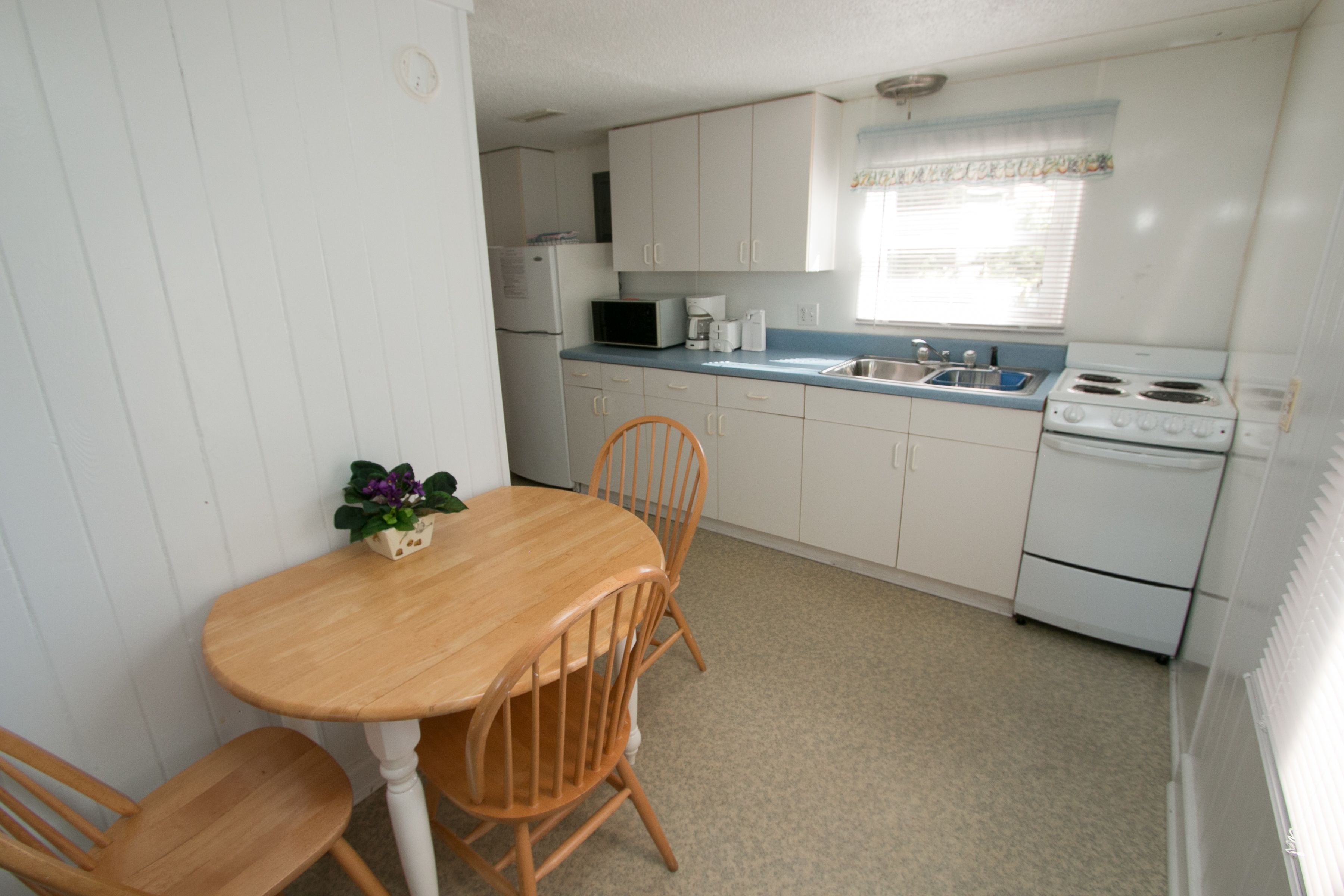 Une cuisine de taille réduite avec des meubles blancs, une table en bois et des chaises.