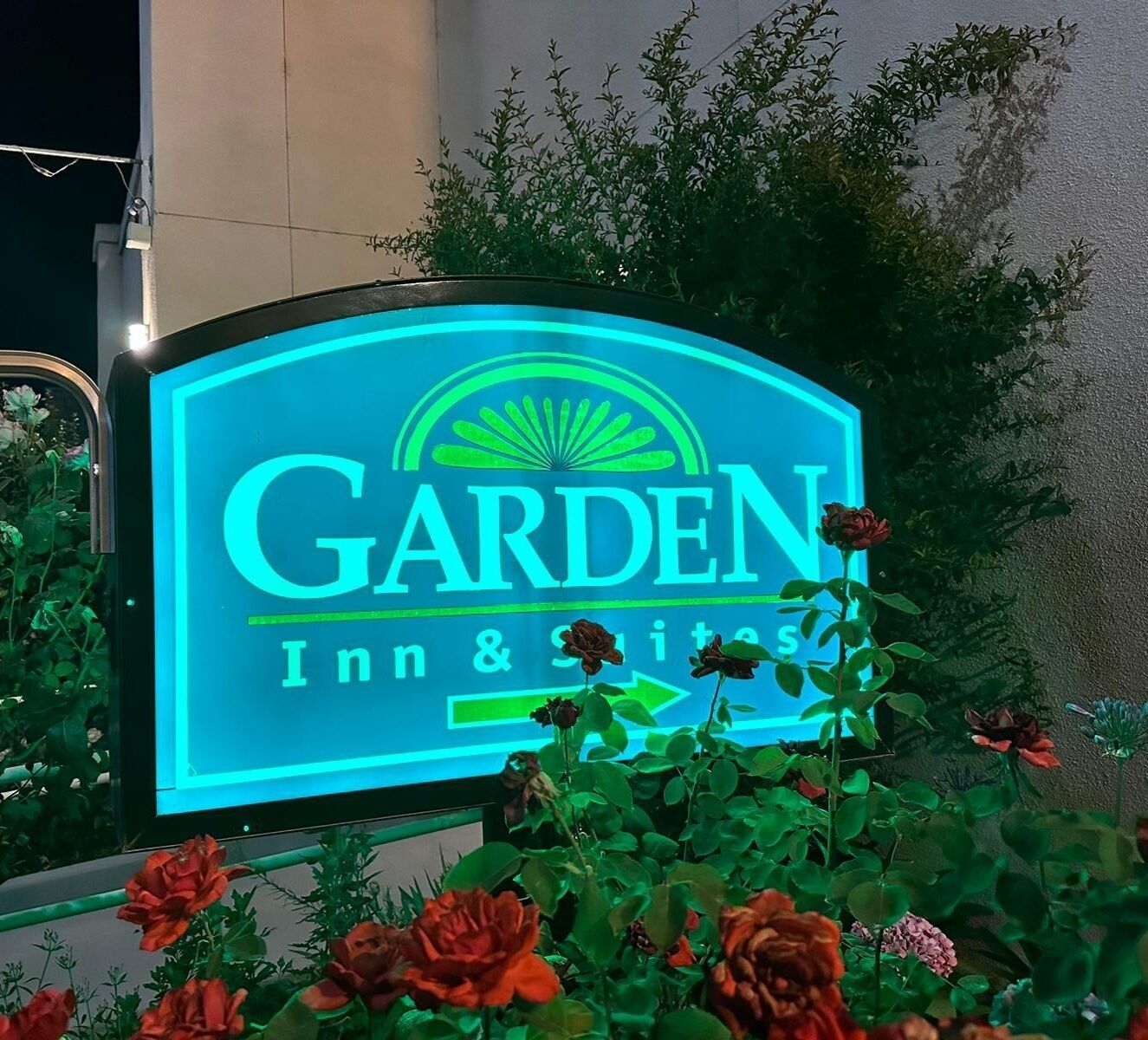 A neon sign for a Garden Inn & Suites hotel, surrounded by flowers.