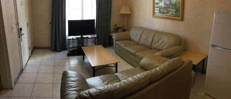 A living area with a sofa, a coffee table, a TV, a lamp, and a painting on the wall.