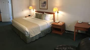 Quarto de hotel com uma cama, duas luminárias de cabeceira, mesa de cabeceira com telefone, escrivaninha com telefone e uma porta.