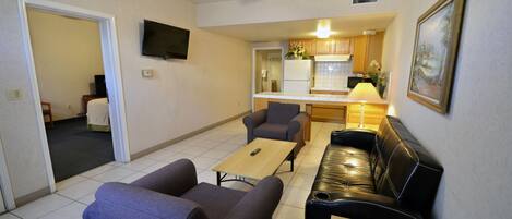 A living room with a sofa, two armchairs, a coffee table, and a TV mounted on the wall.
