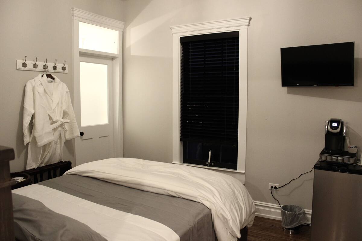 Une chambre à coucher avec un lit, une télévision, une machine à café et une fenêtre avec des stores.