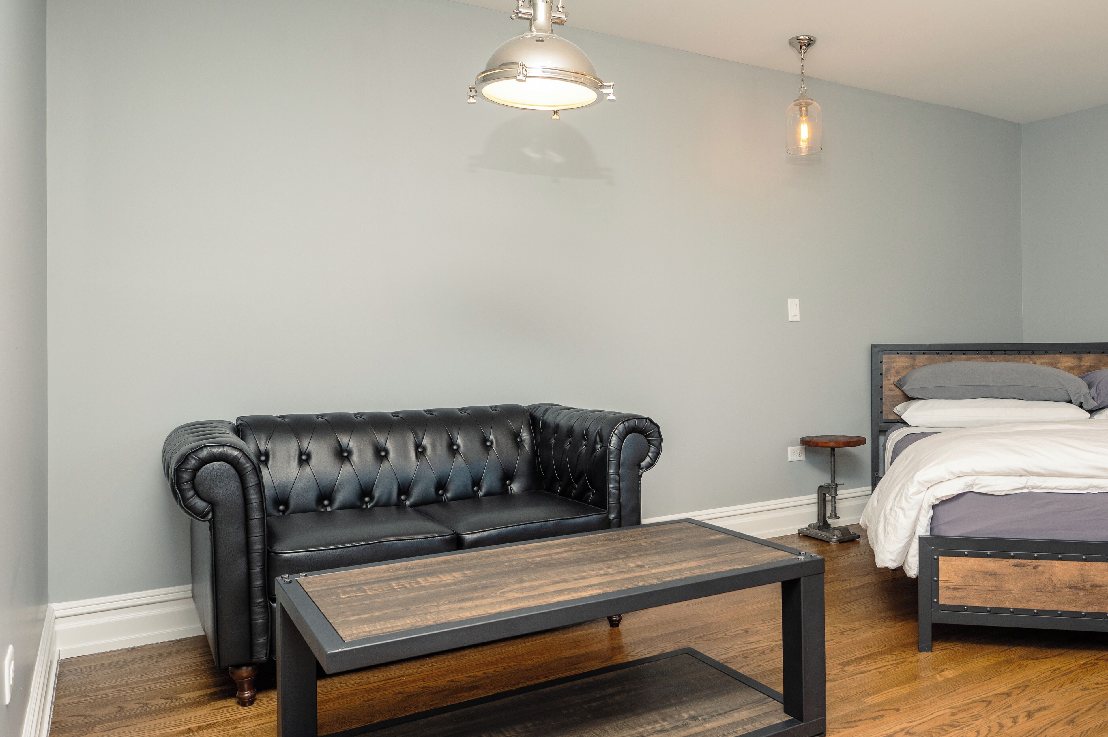 Una habitación con un sofá de cuero negro, una mesa de centro de madera, una cama con estructura de madera y una lámpara colgante.