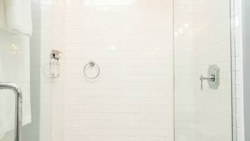 A glass-enclosed shower with white hexagonal tiles, a glass door, and a towel on the floor.