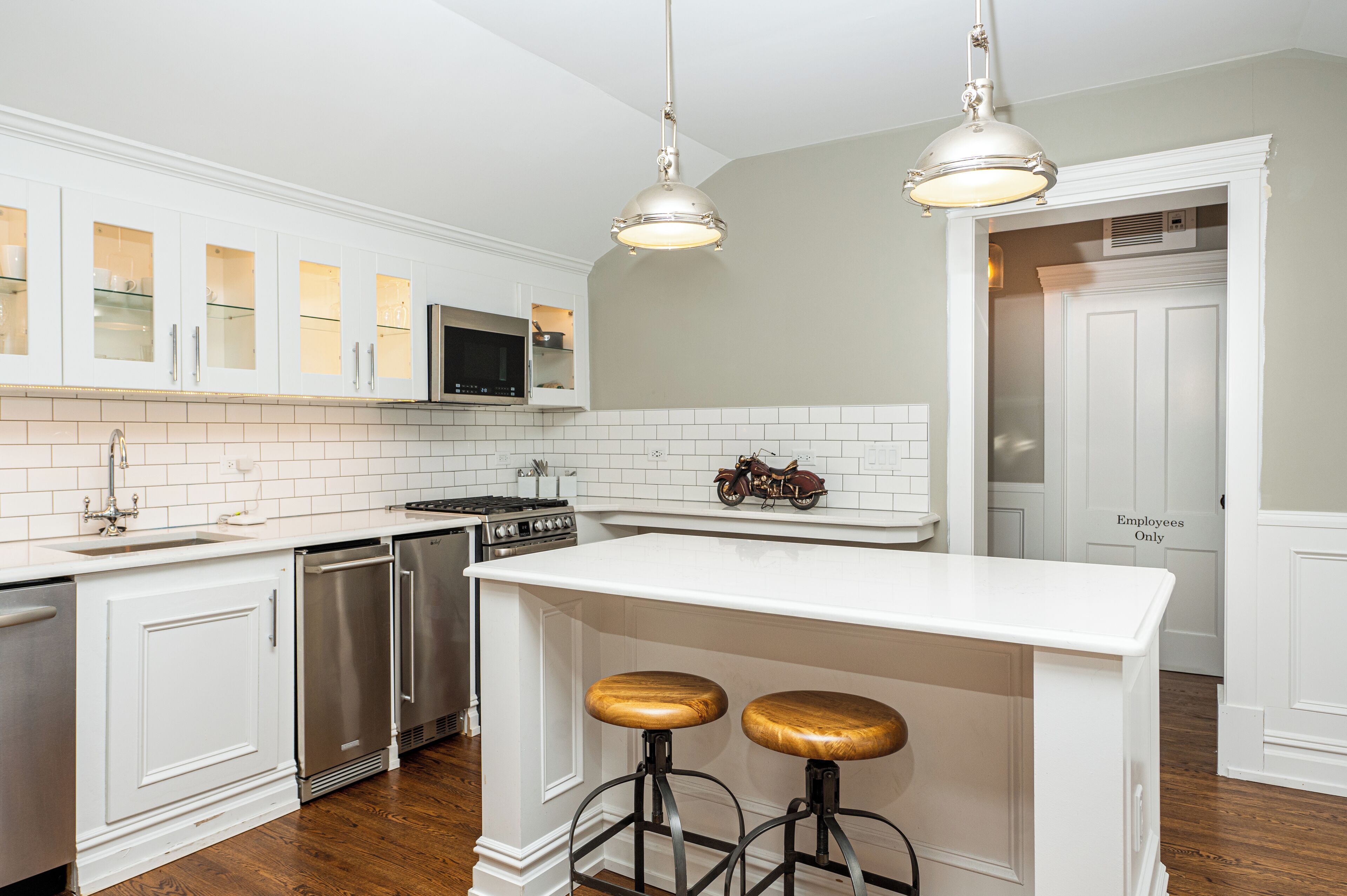 A kitchen with white cabinetry, stainless steel appliances, and a bar stool.