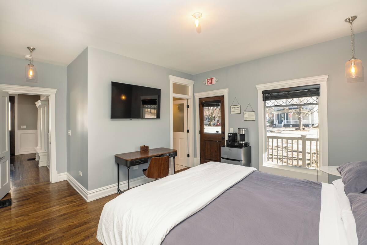 Une chambre à coucher comprenant un lit, un bureau, une chaise, un téléviseur et une fenêtre donnant sur l’extérieur.