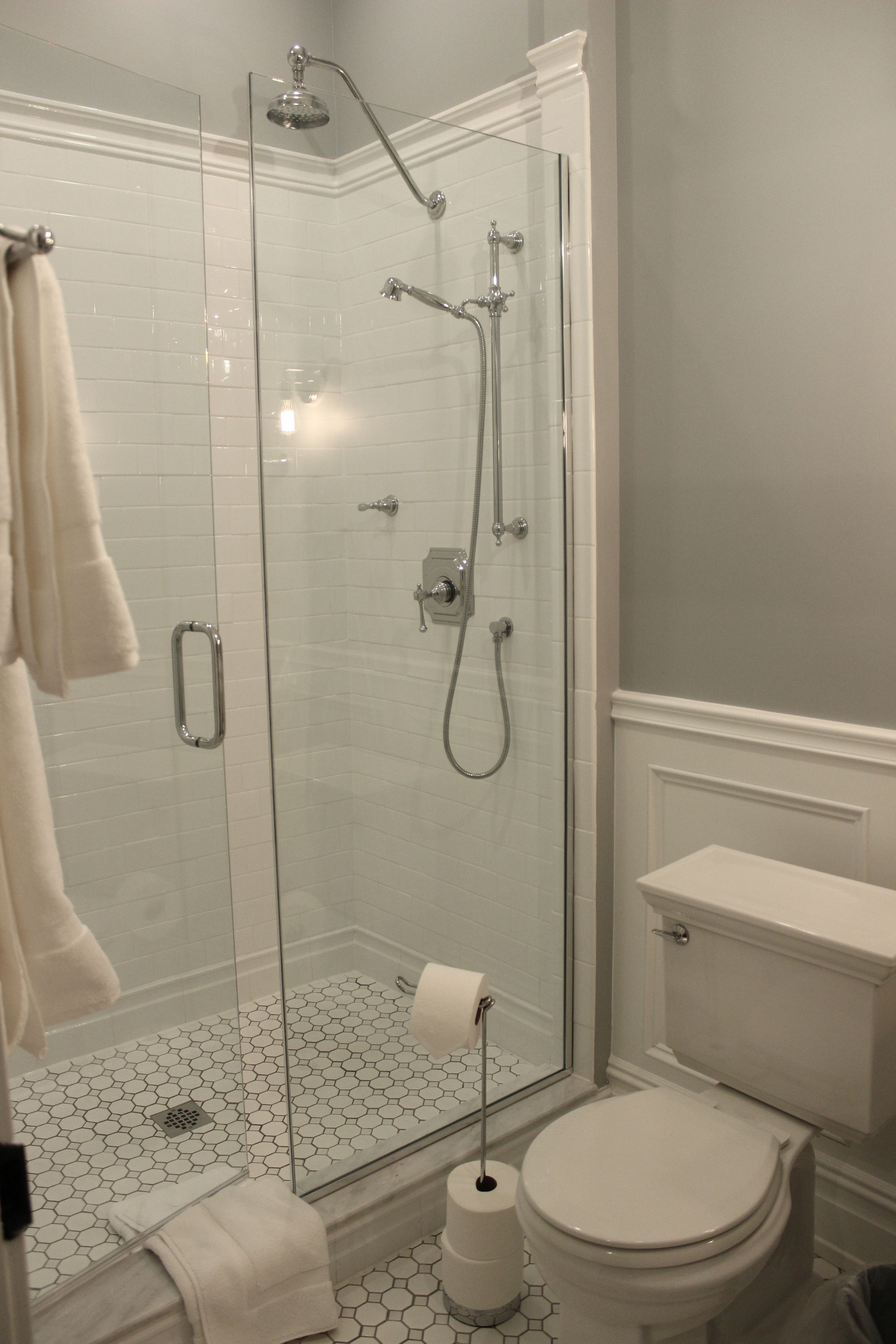 Une salle de bain avec une douche à parois de verre, des toilettes et un sol carrelé de couleur blanche.
