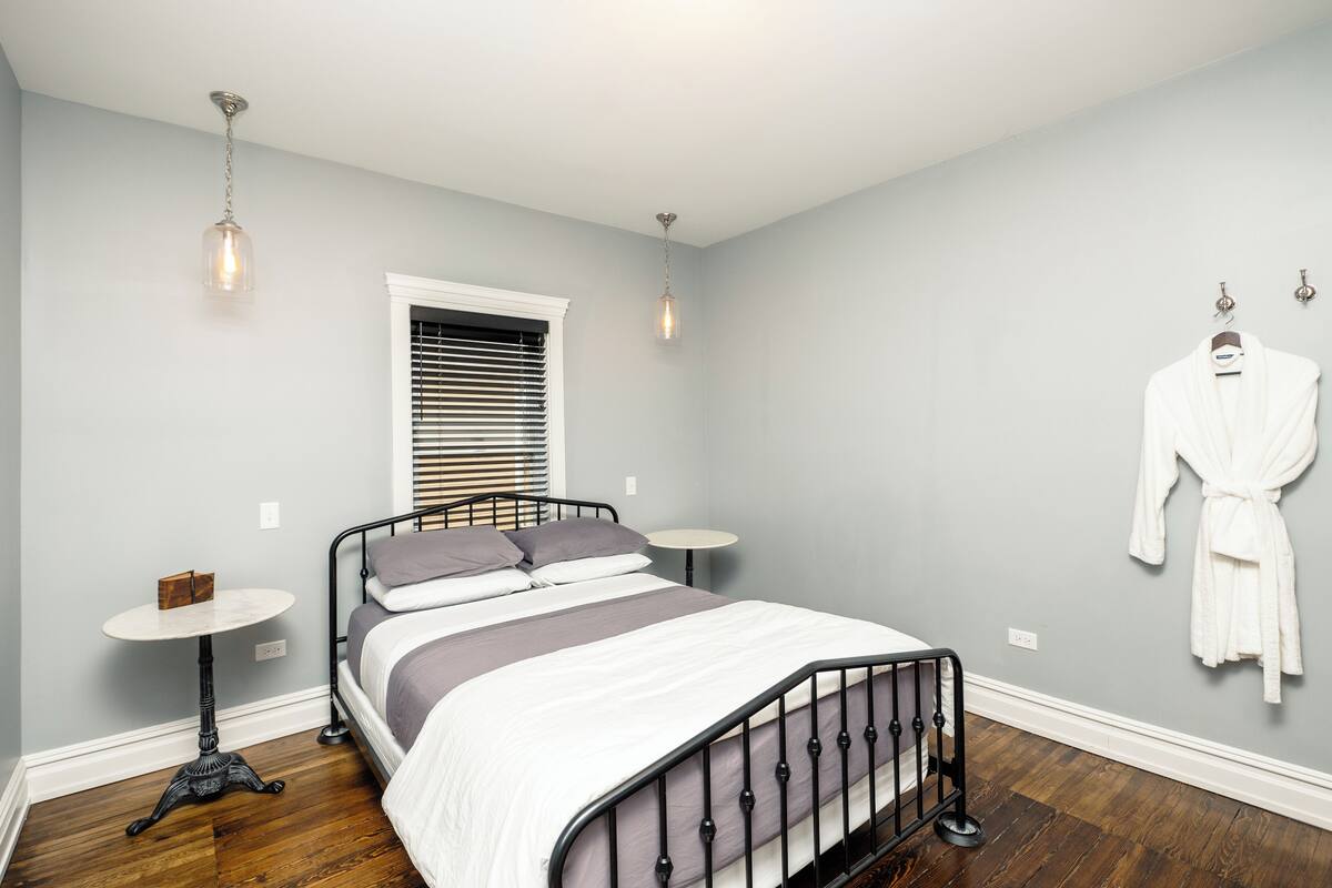 Une chambre à coucher avec un lit, une table de chevet, un porte-manteau et une fenêtre avec des stores.