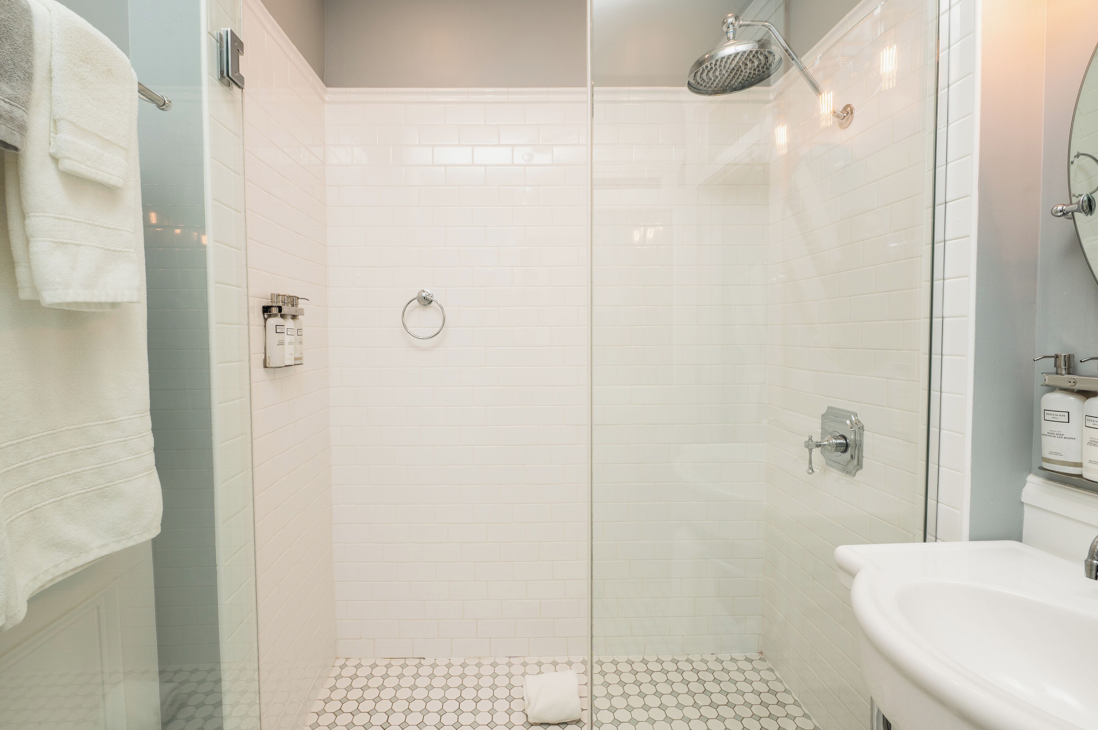 Uma casa de banho moderna com cabine de duche em vidro, lavatório branco e chão em azulejos.
